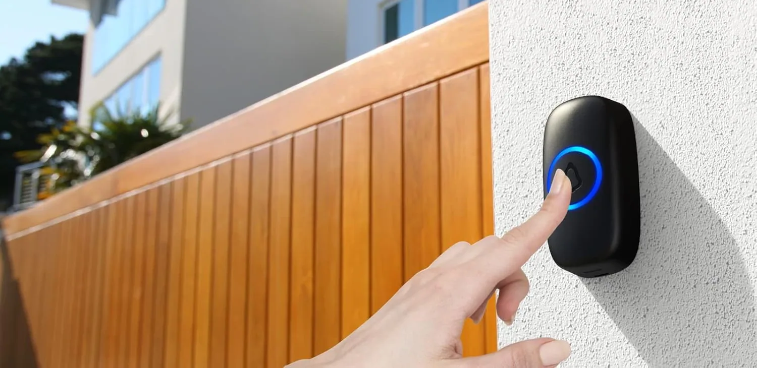 A SECRUI doorbell button on a wall beside a wooden garden fence